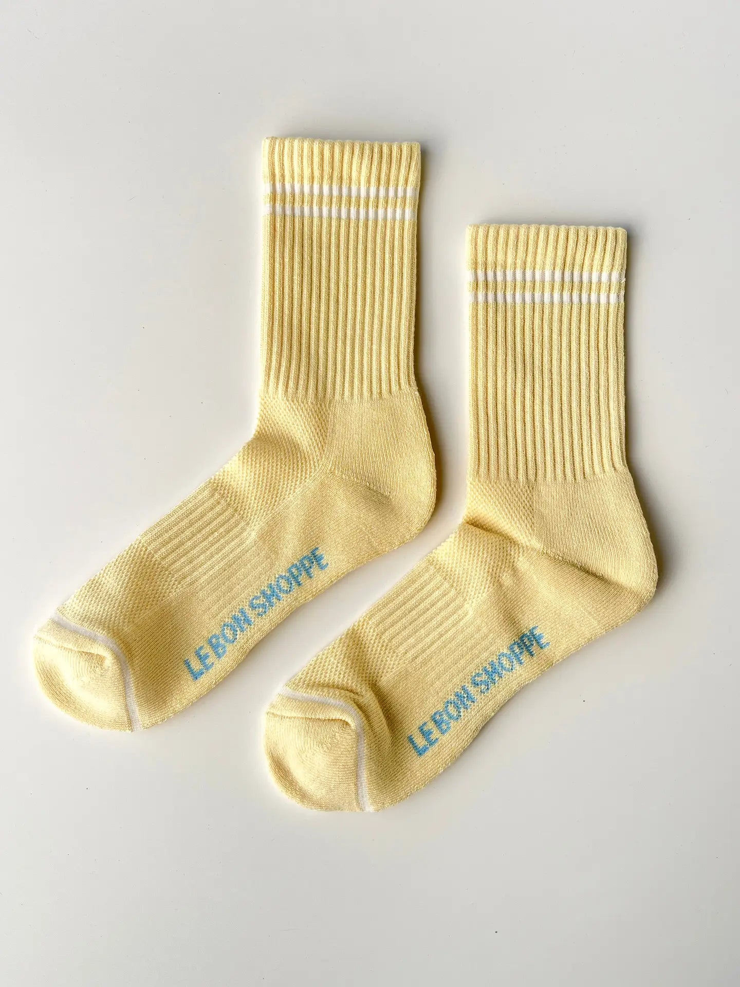 Pair of yellow socks with 'Le Bon Shoppe' branding on a light gray background