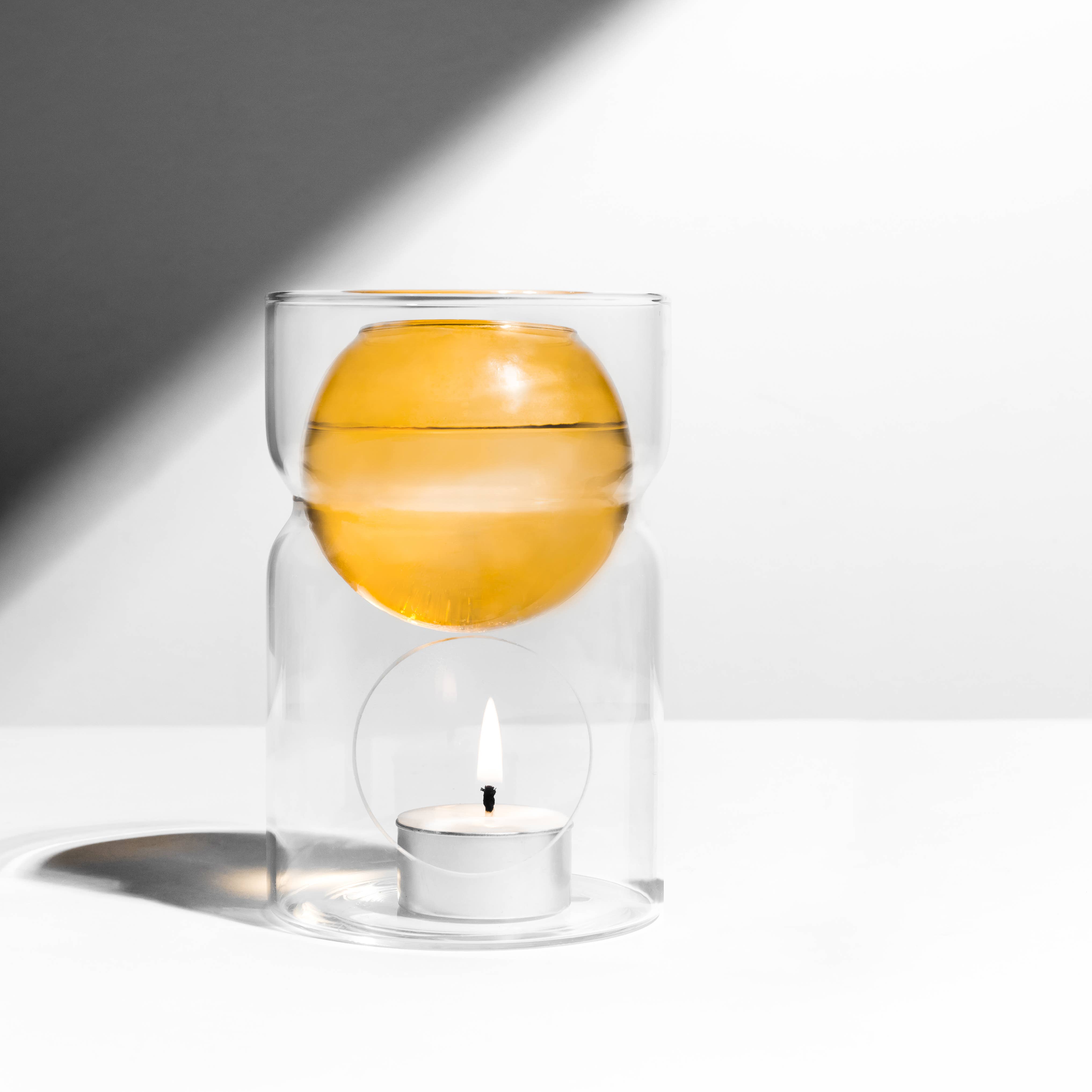 Glass container with a floating orange and a candle inside on a white background