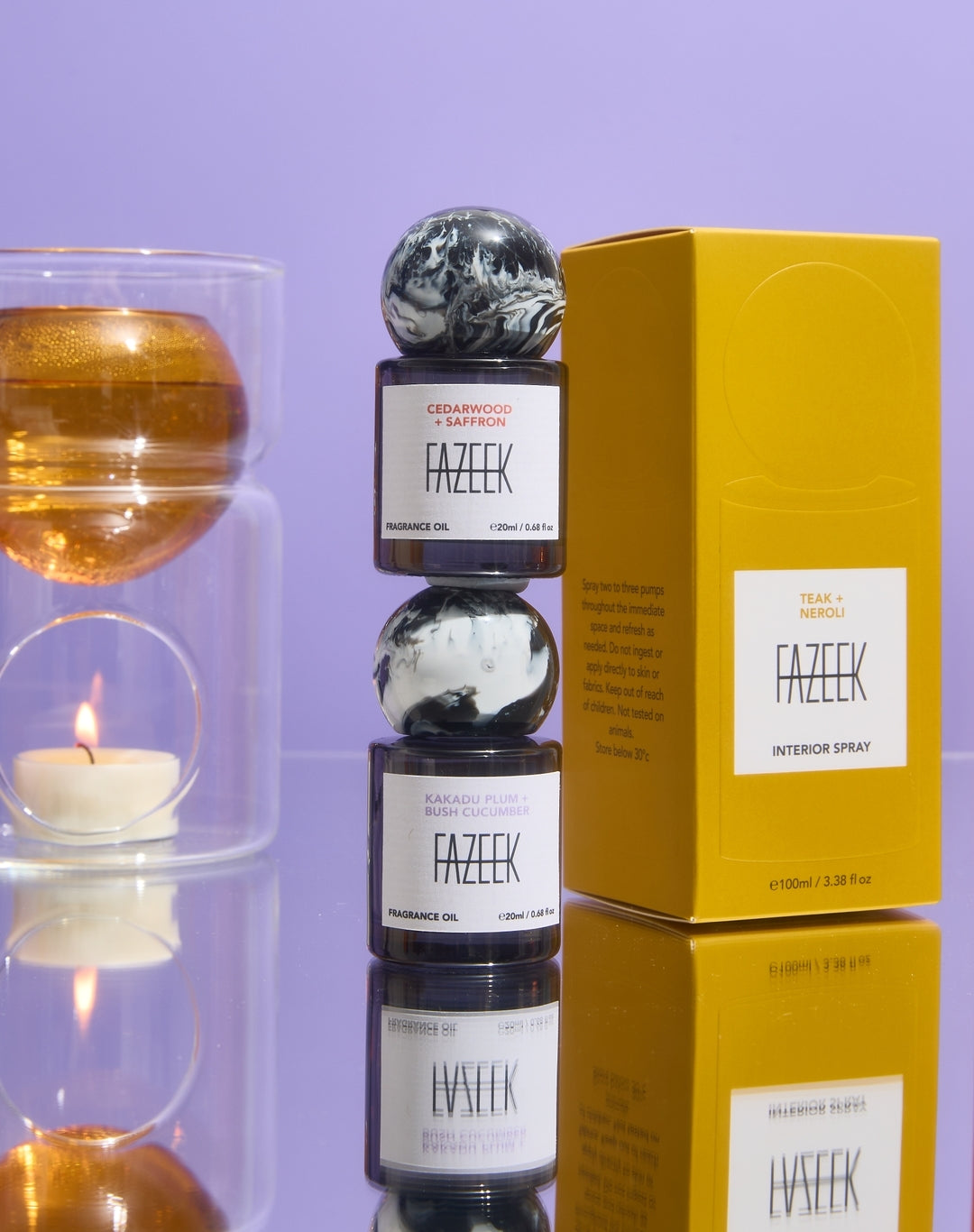 Fazeek fragrance oil bottles with marble-patterned caps stacked next to a yellow box, with a lit candle and glass vessel in the background against a lavender backdrop.