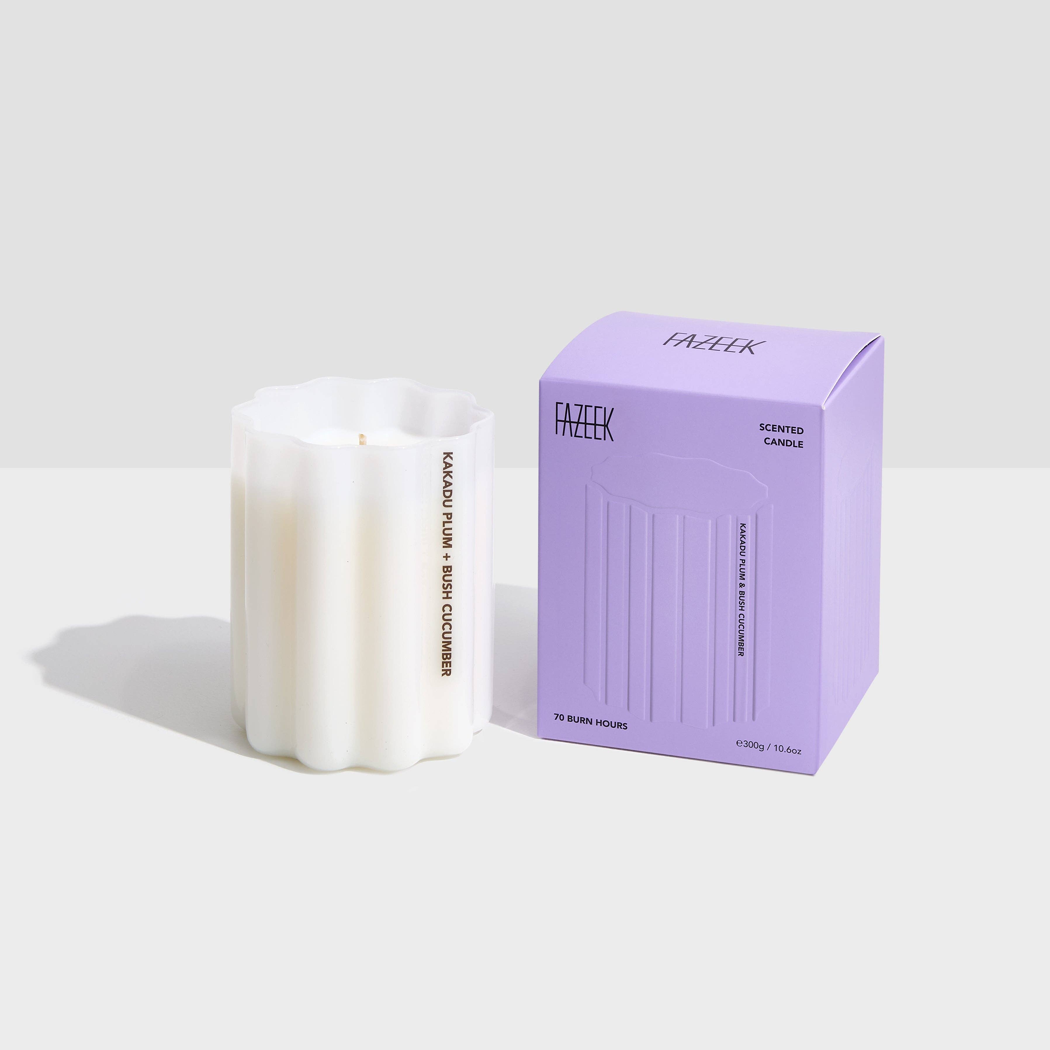 A white ribbed glass candle next to its lavender purple packaging box, both featuring the brand name 'FAZEEK' on a clean light gray background.