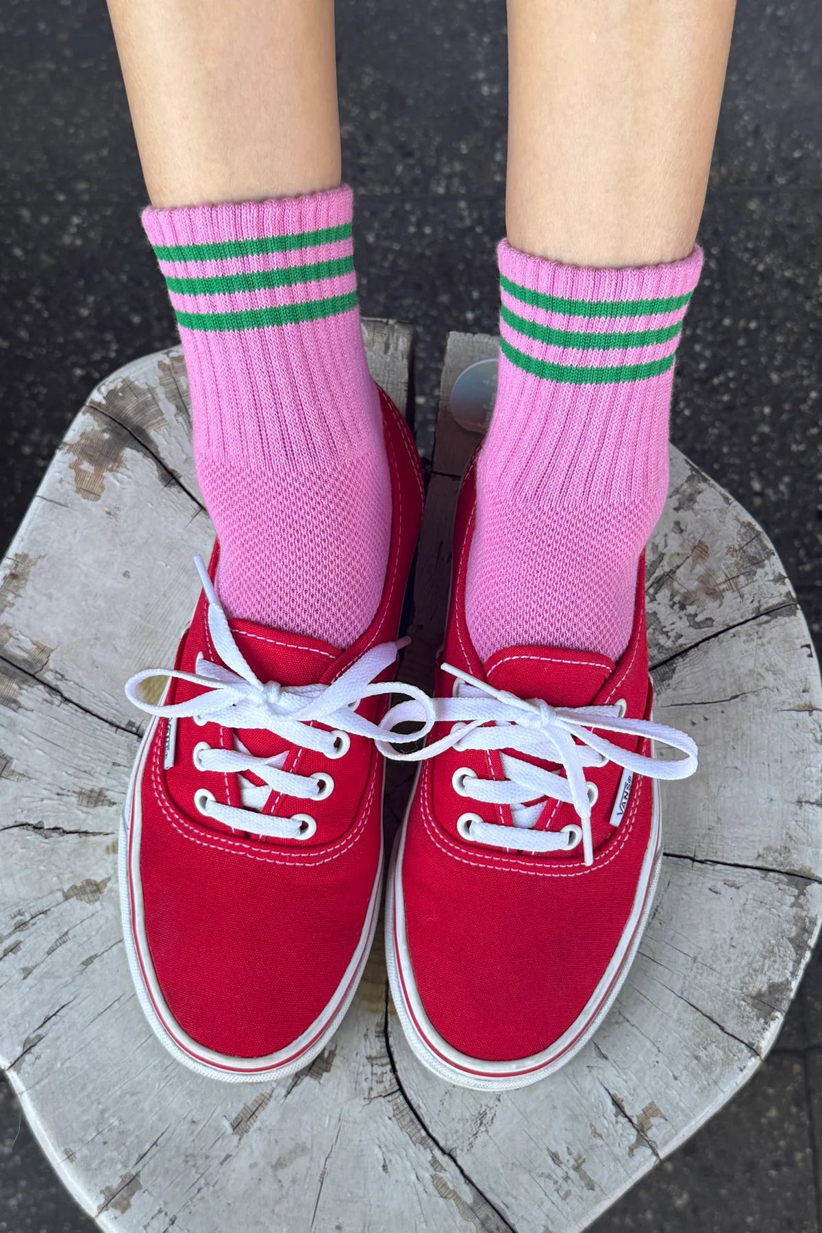 Red sneakers with white laces worn with pink socks featuring green stripes on a wooden block.