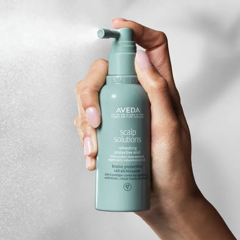 Hand holding a bottle of Aveda scalp solution against a neutral background
