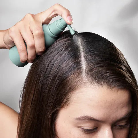 Person using a teal hair product applicator on their hair against a neutral background
