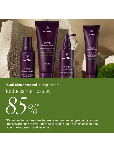 Four Aveda Invati Ultra Advanced haircare products in dark purple packaging are displayed against a textured stone background, with a green text banner below featuring promotional copy about reducing hair loss by 85%.