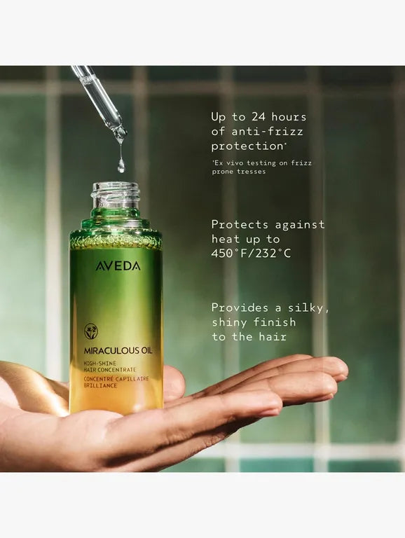 Aveda miraculous oil bottle with dropper held by a hand, against a blurred bathroom background.