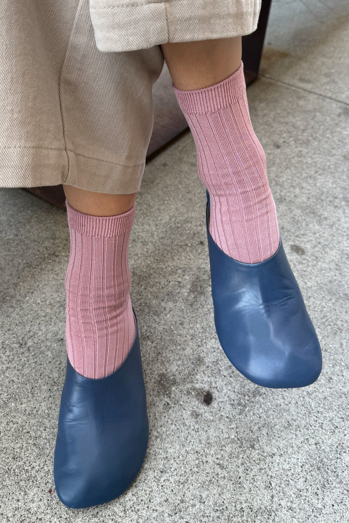 Person wearing pink socks and blue shoes on a concrete floor