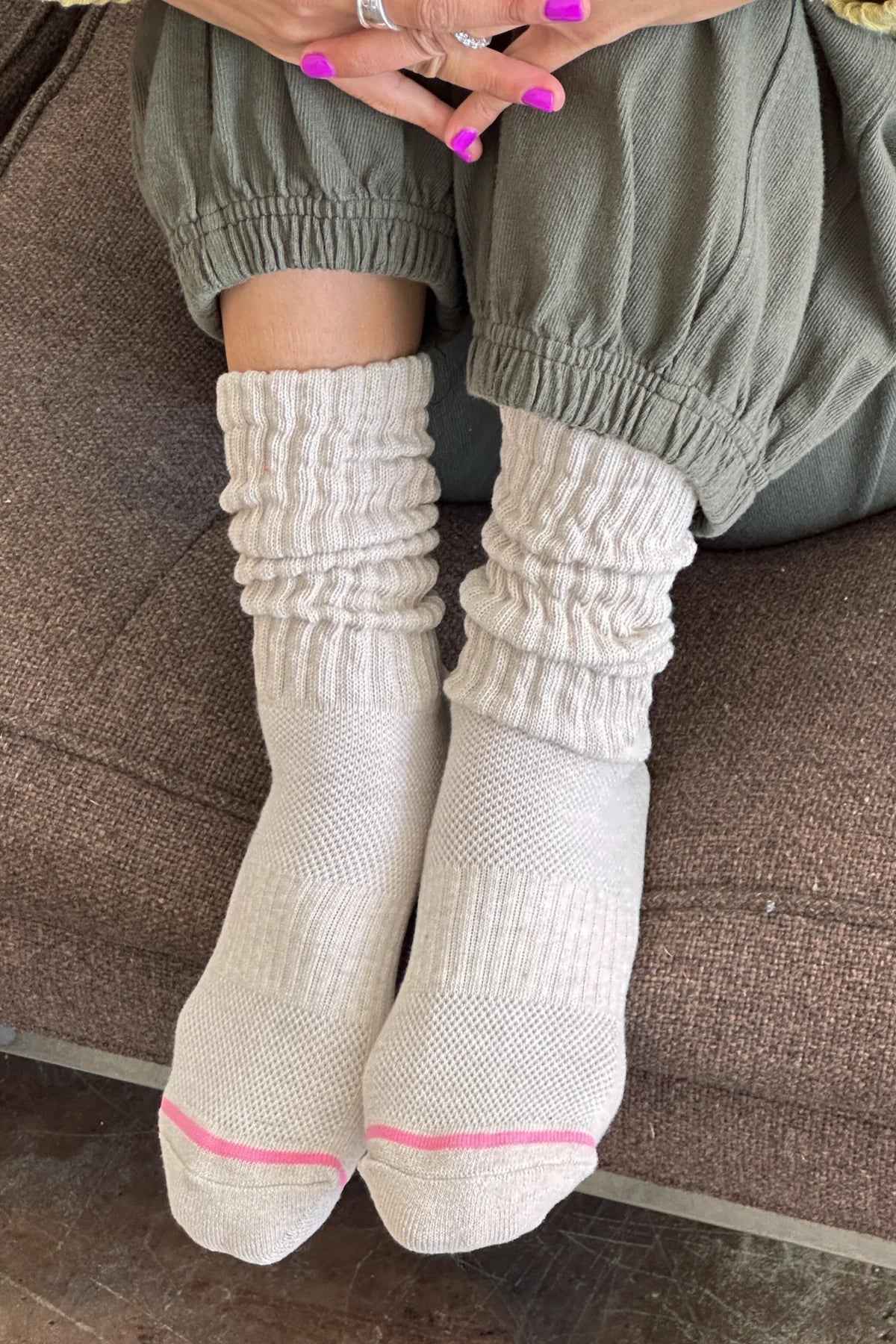 Person wearing beige socks with pink accents on a brown couch.