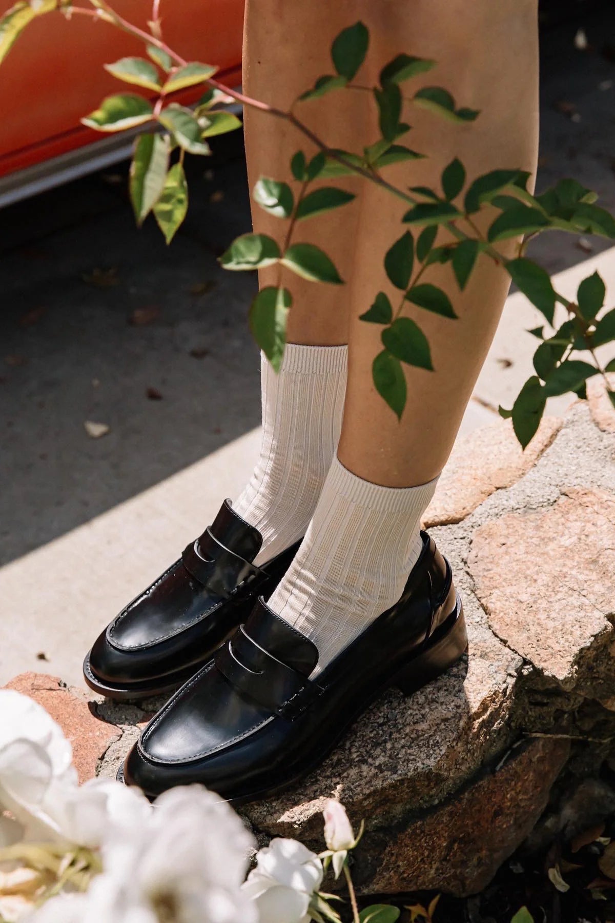 Person wearing black shoes and white socks standing on a stone surface with greenery around.