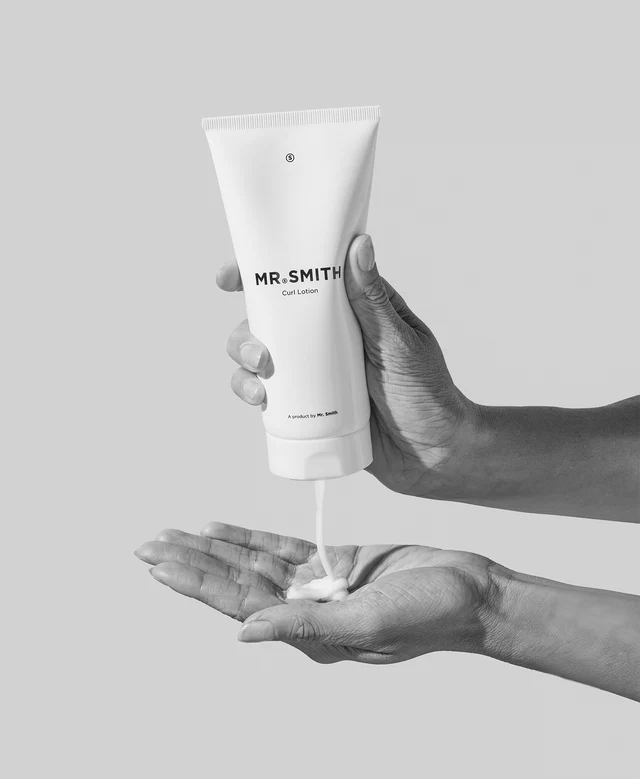 Hand holding a tube of 'MR. SMITH' lotion against a gray background