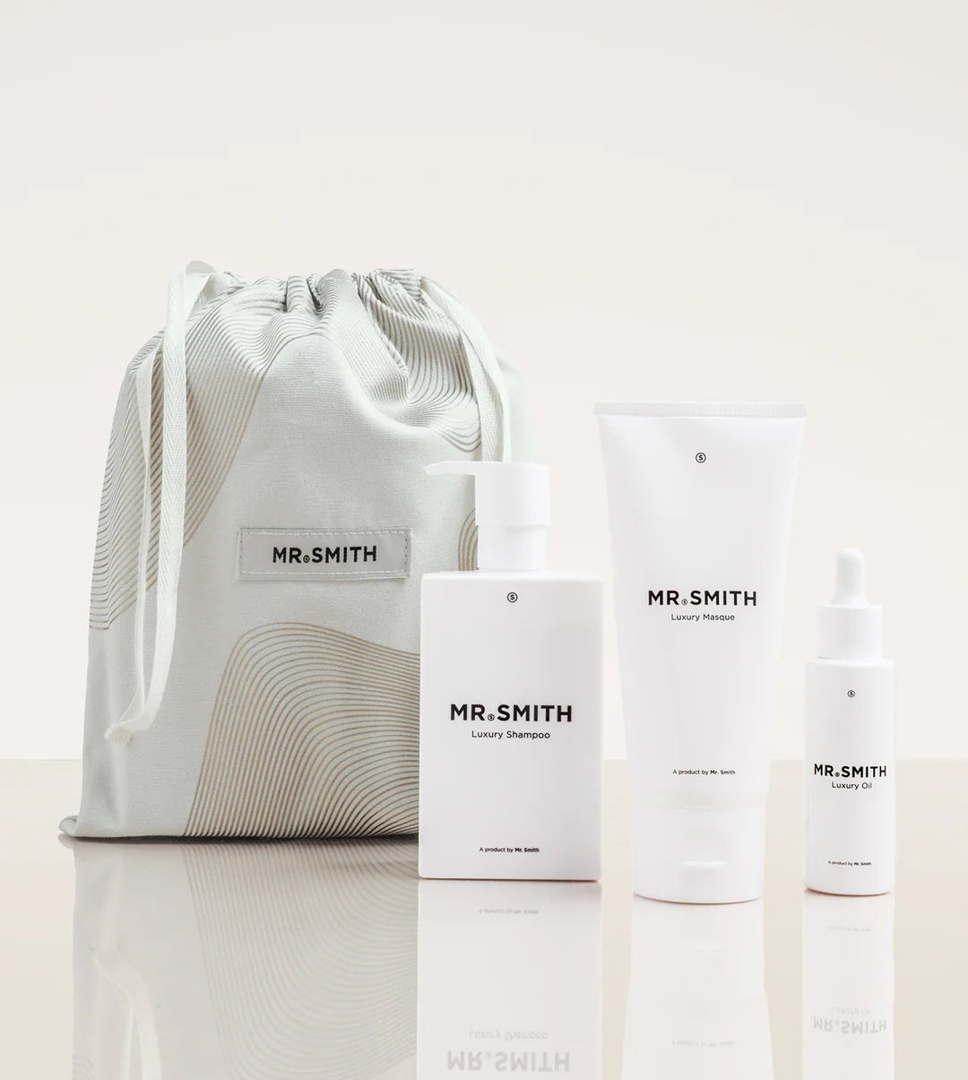 A set of white Mr. Smith skincare products and a drawstring bag on a reflective light beige surface.