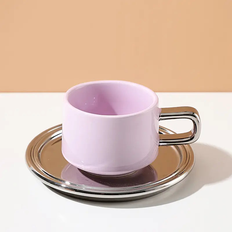Pink ceramic cup with silver handle on a matching saucer against a beige background