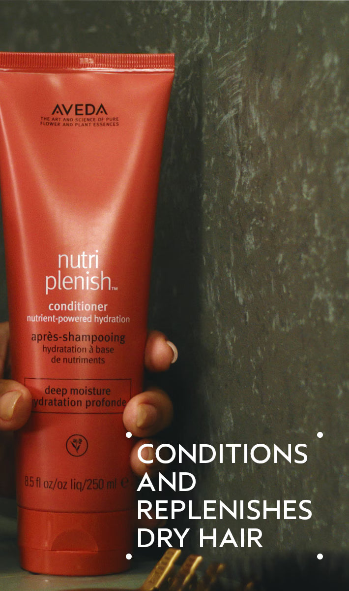 Aveda Nutriplenish conditioner bottle held by a hand with a dark background