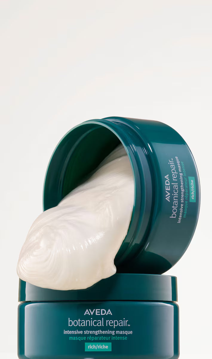 A jar of Aveda Botanical Repair intensive strengthening mask with its lid open, showing a thick, creamy off-white mask being dispensed, set against a clean white background.
