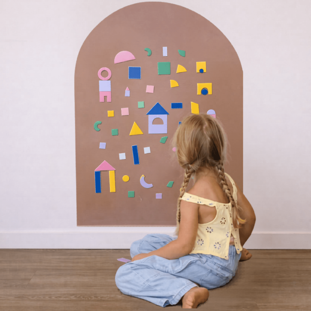 Child sitting on the floor in front of a wall with colorful geometric shapes.