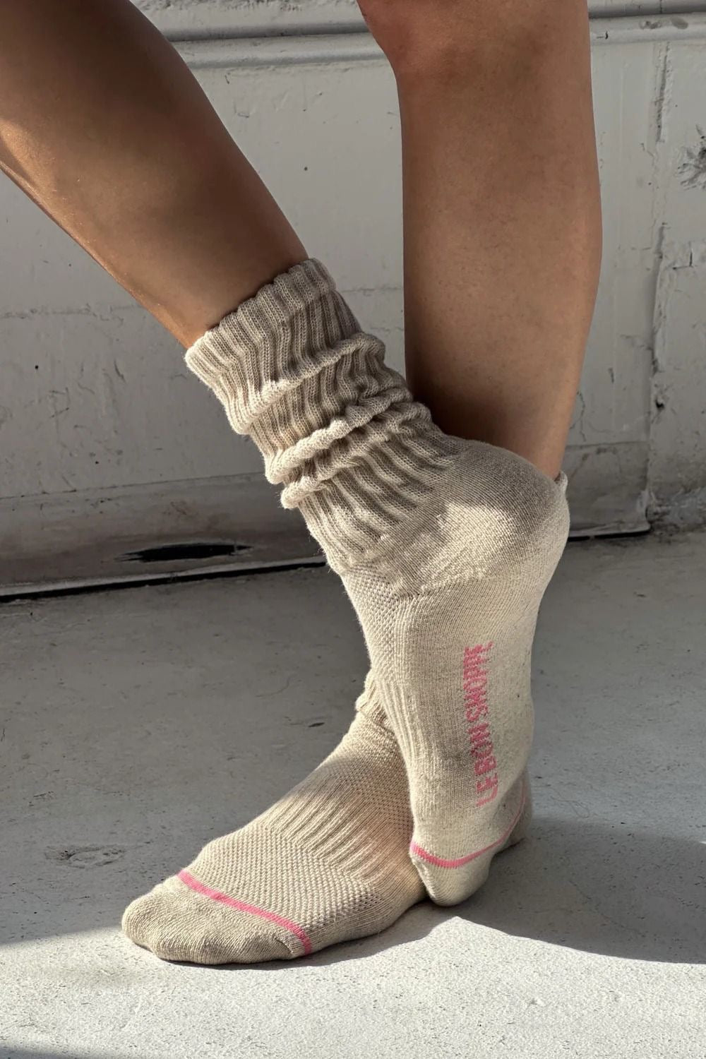 Beige socks with pink text worn by a person on a light gray floor.