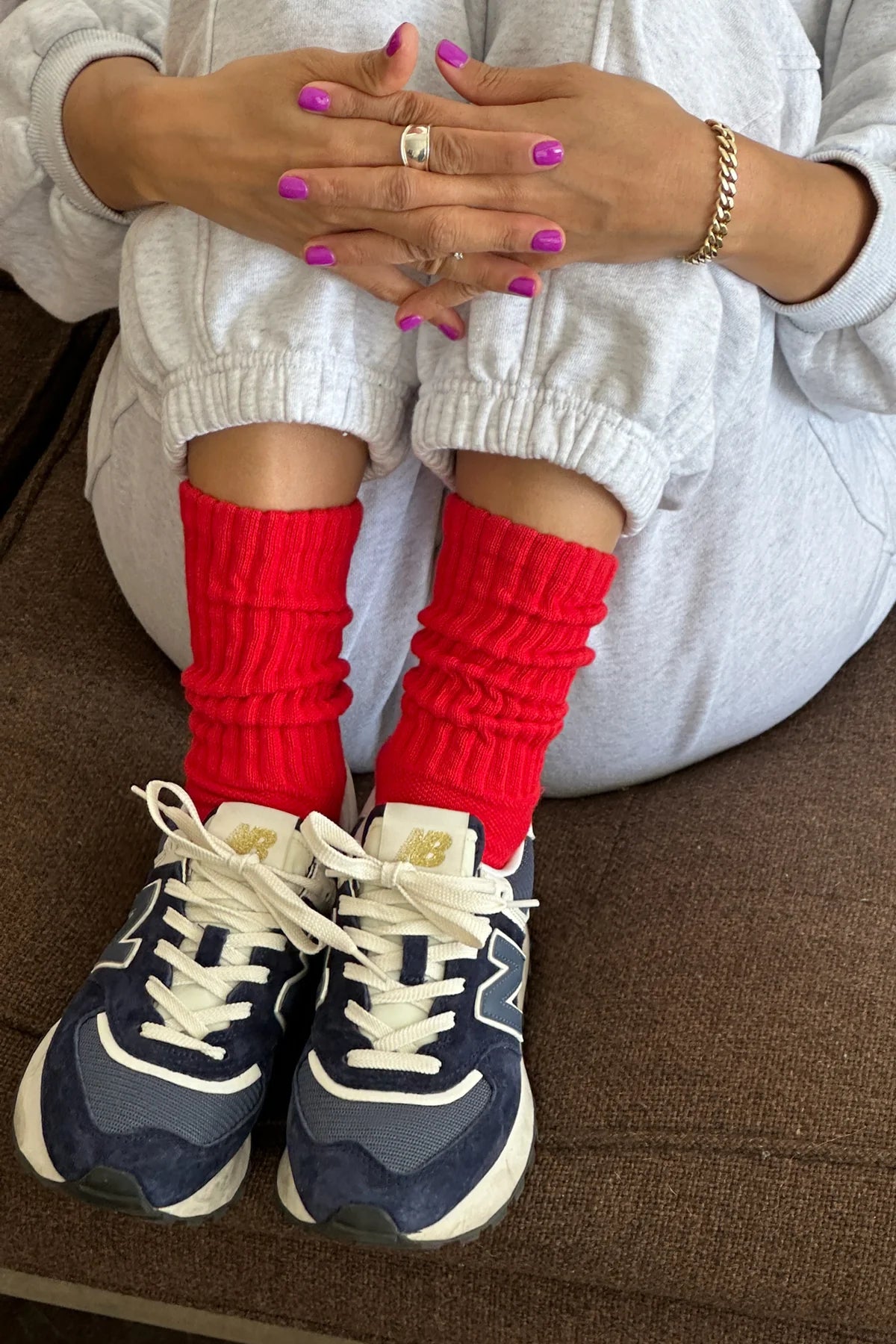 Person wearing red socks and navy sneakers on a brown couch.