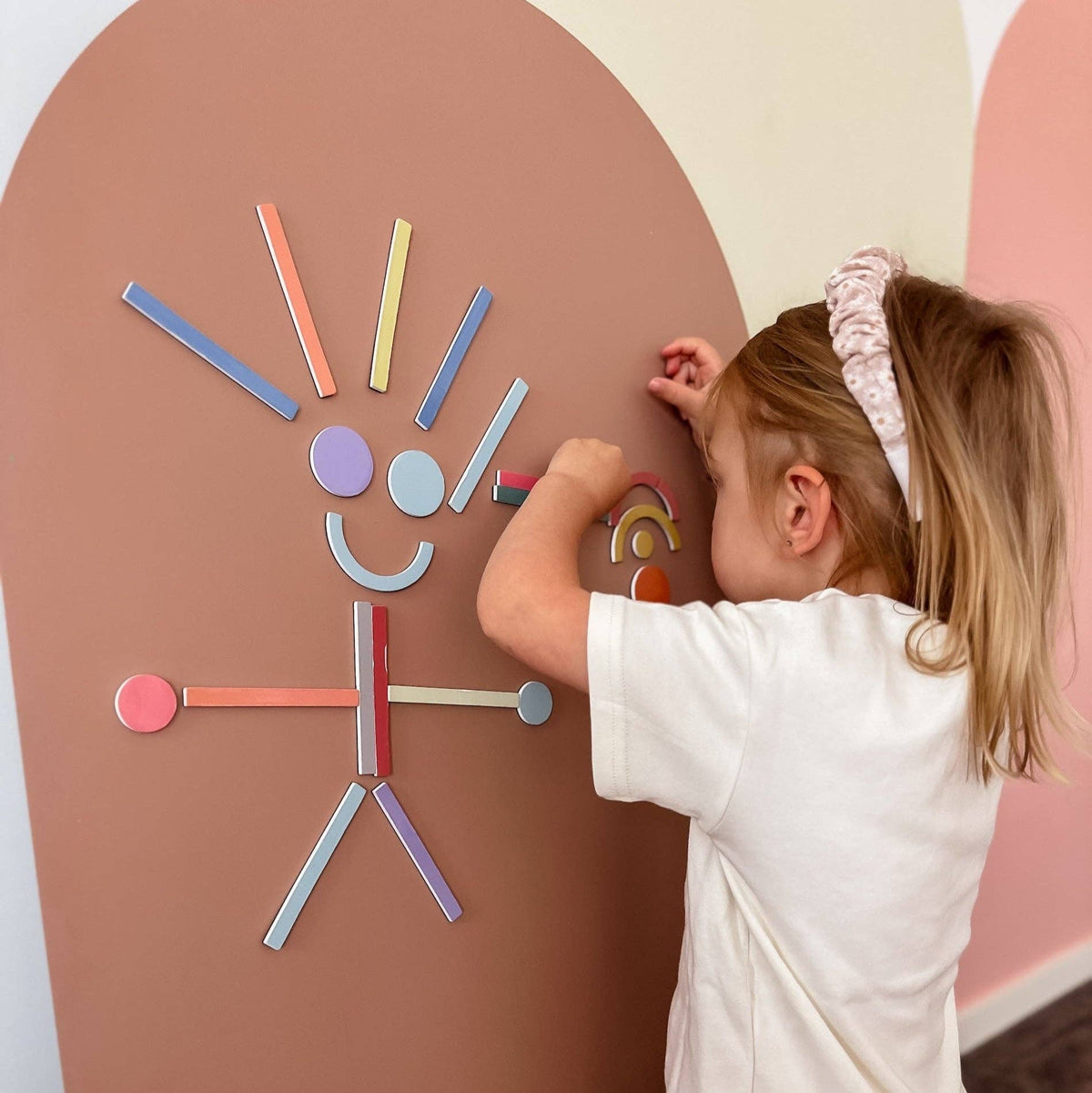 Child playing with a colorful wall art made of magnetic pieces on a brown background