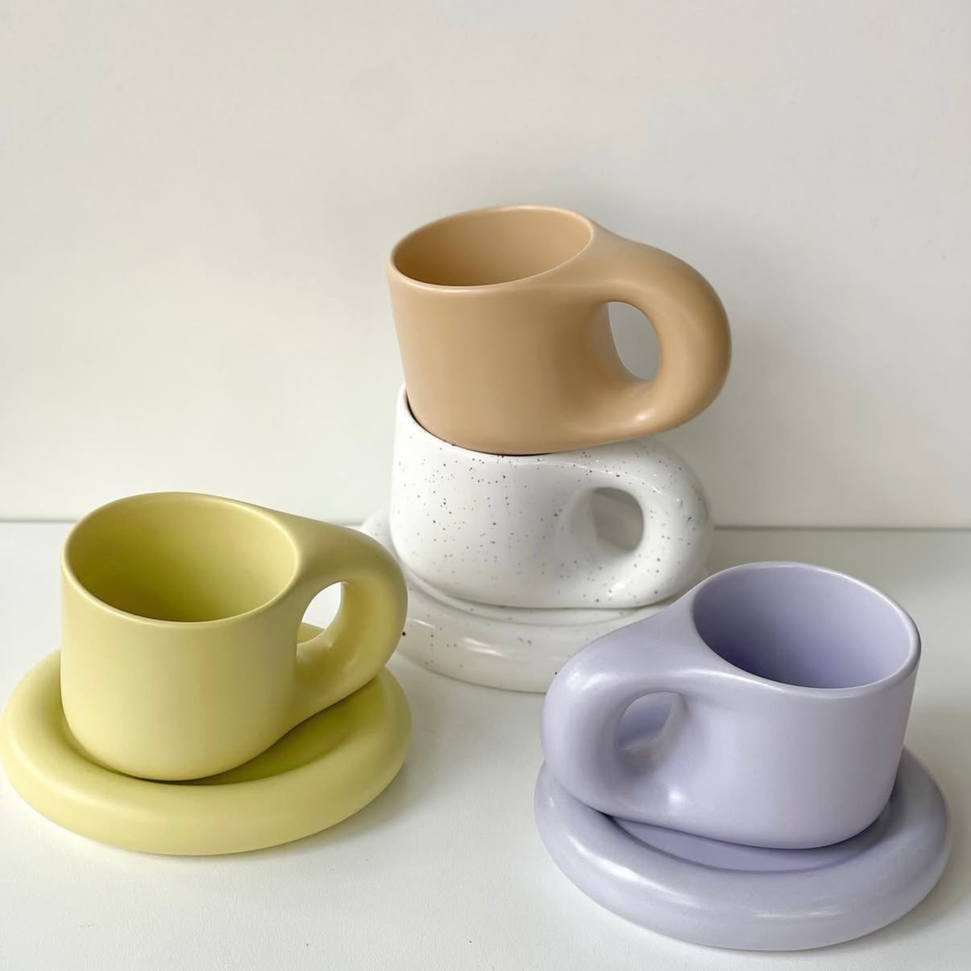 Set of ceramic mugs and coasters in beige, green, and purple on a white surface.