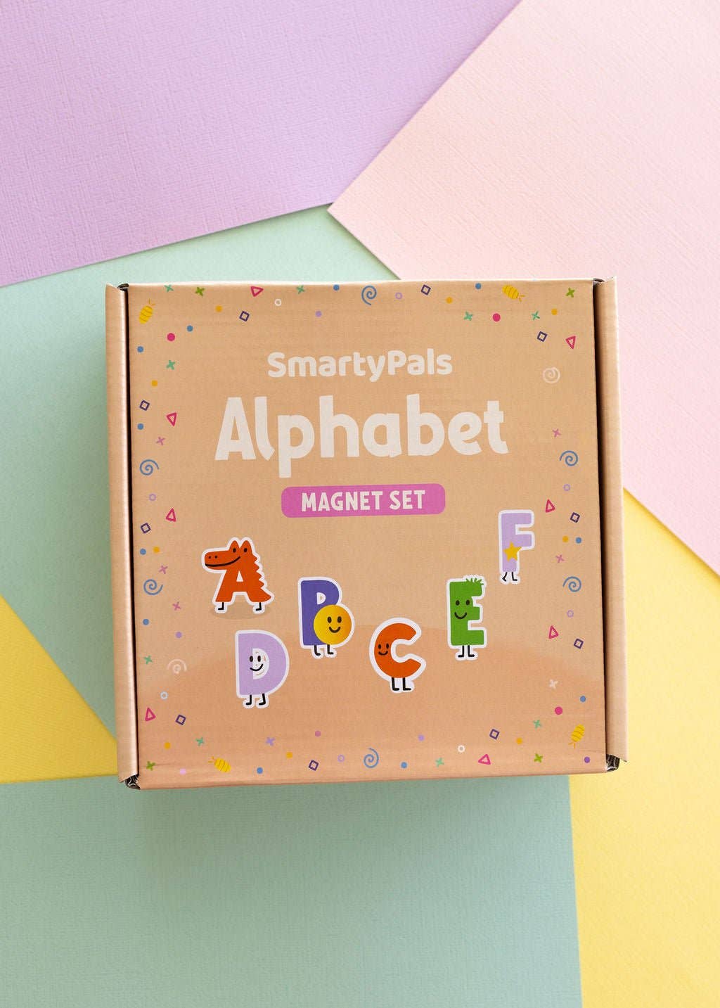 A cardboard box for the SmartyPals Alphabet Magnet Set, decorated with colorful cartoon letters and confetti on a pastel geometric background.
