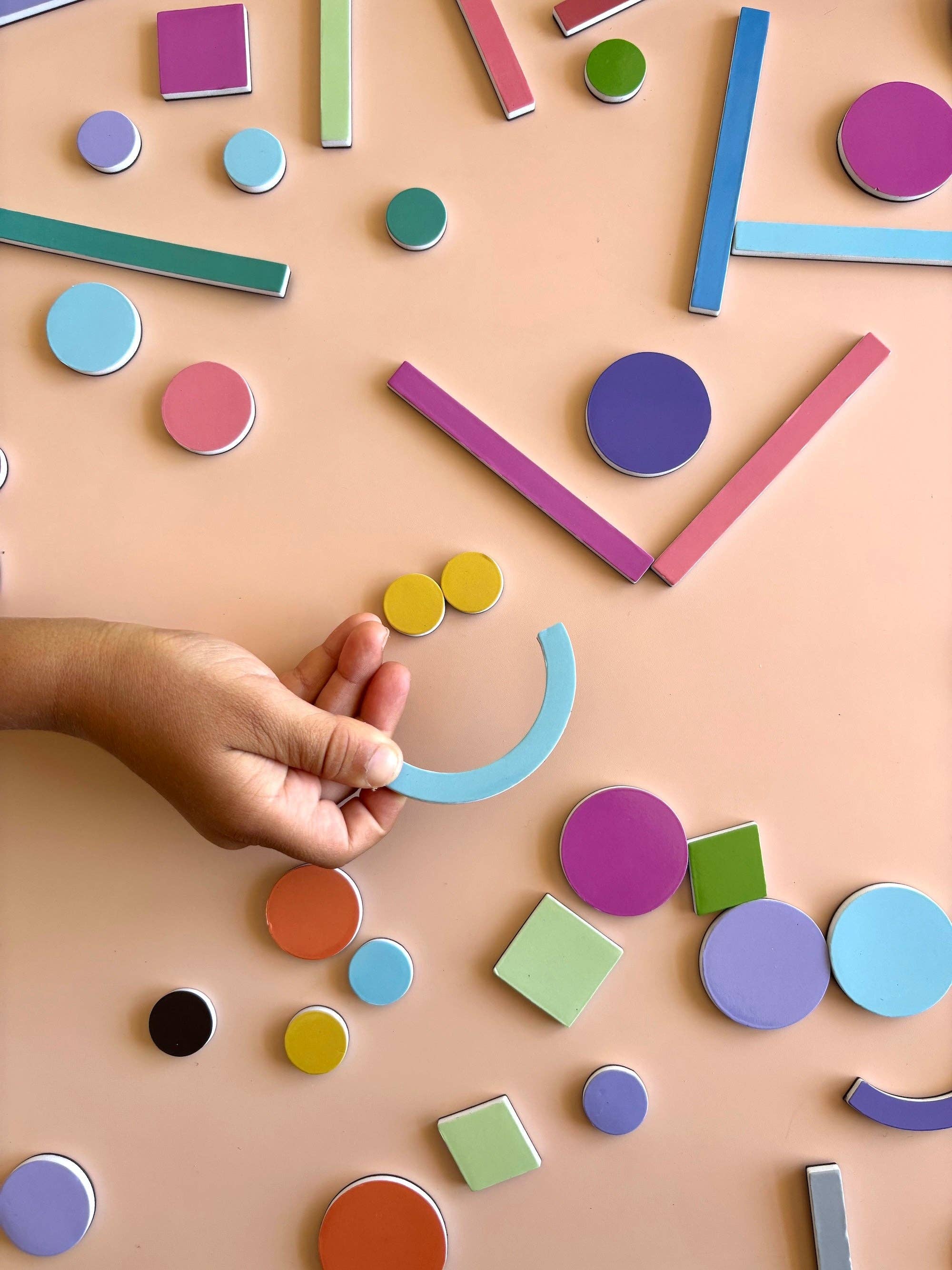 Colorful geometric shapes on a beige surface with a hand interacting with them.