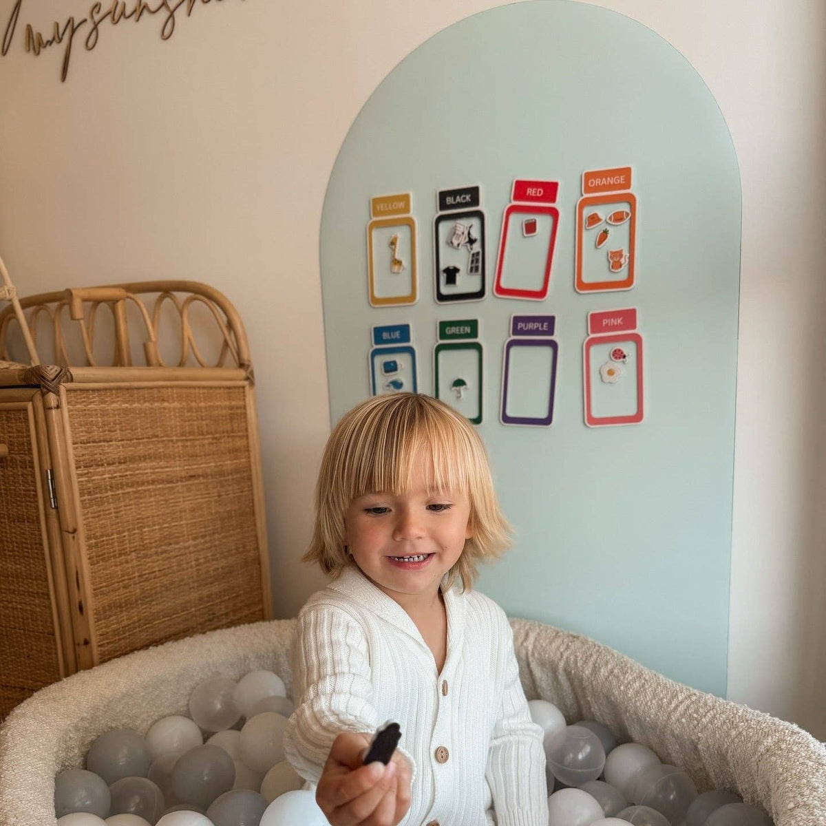 Child playing with a remote control in a ball pit with educational wall posters in the background.