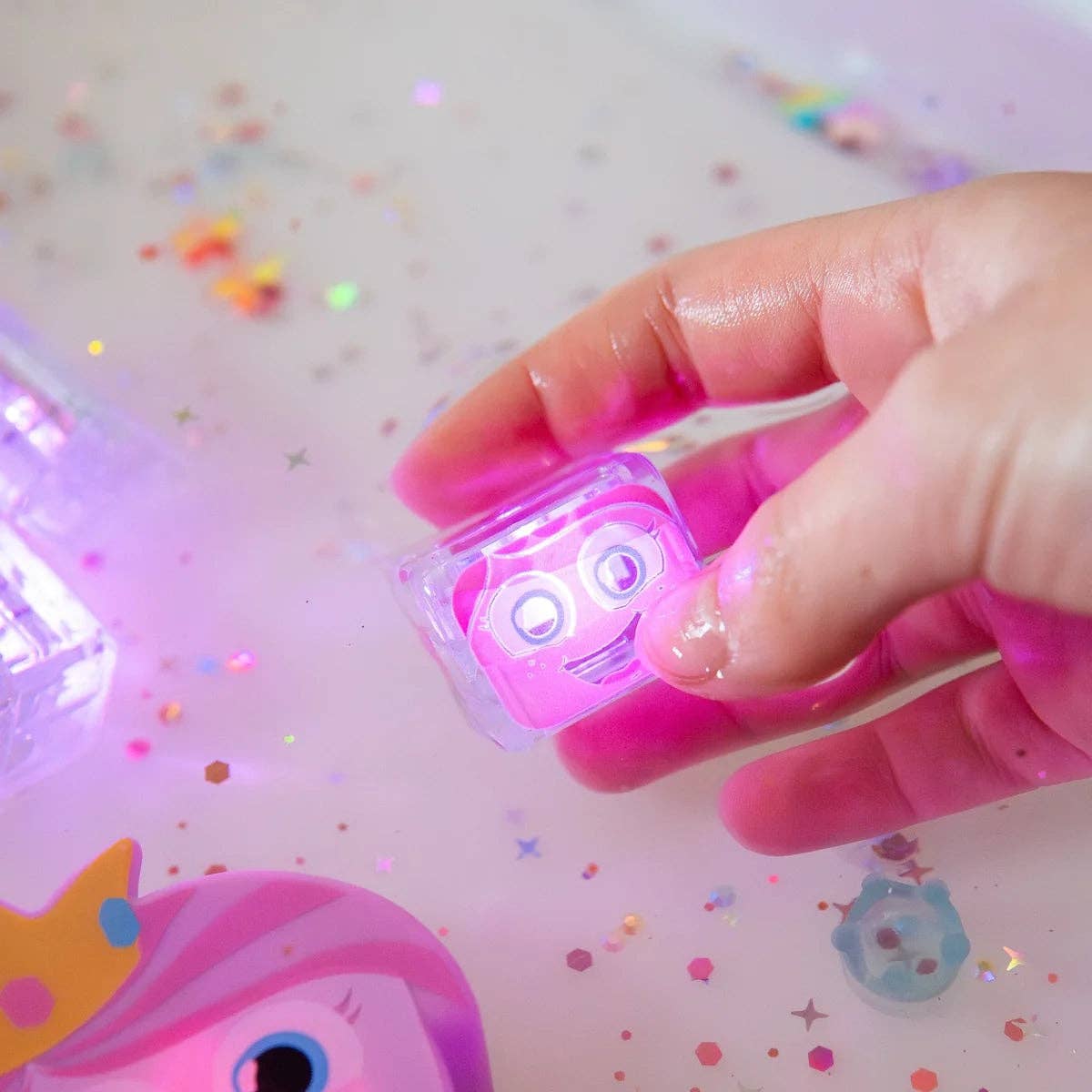 Hand holding a small pink toy with a face on a colorful background