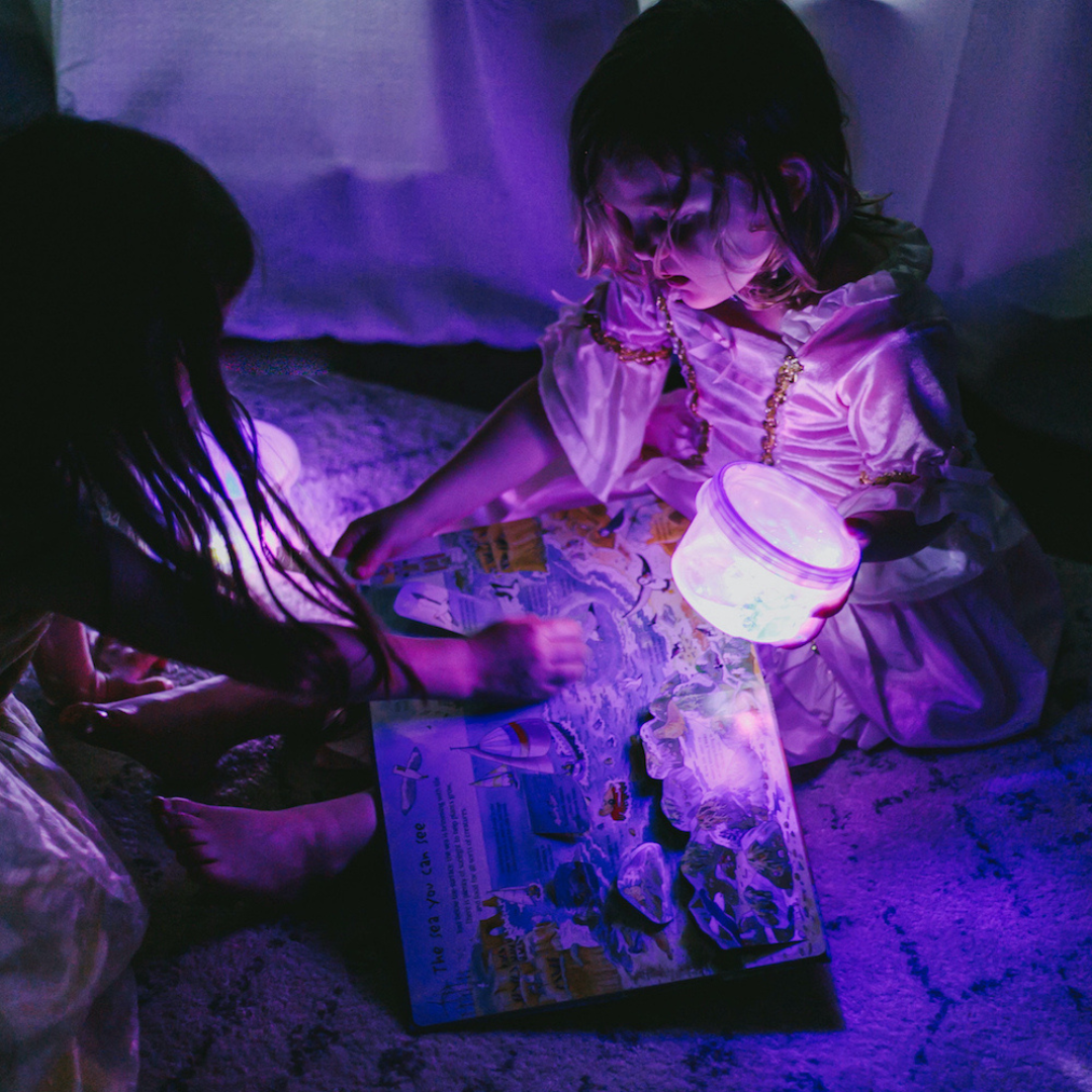 Two children in a dimly lit room with a glowing lantern and book.