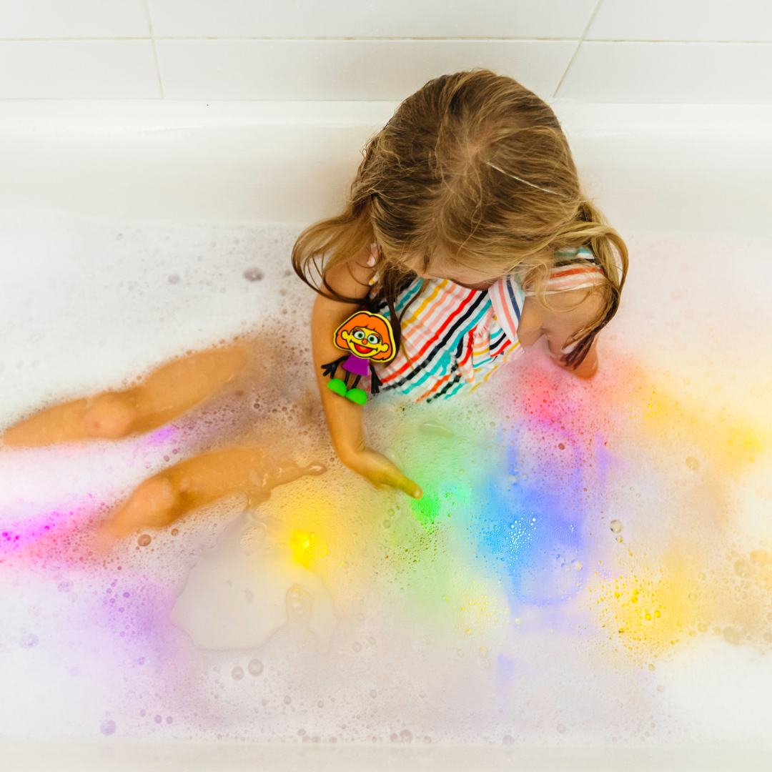Child in a bathtub filled with colorful bath bombs and bubbles.