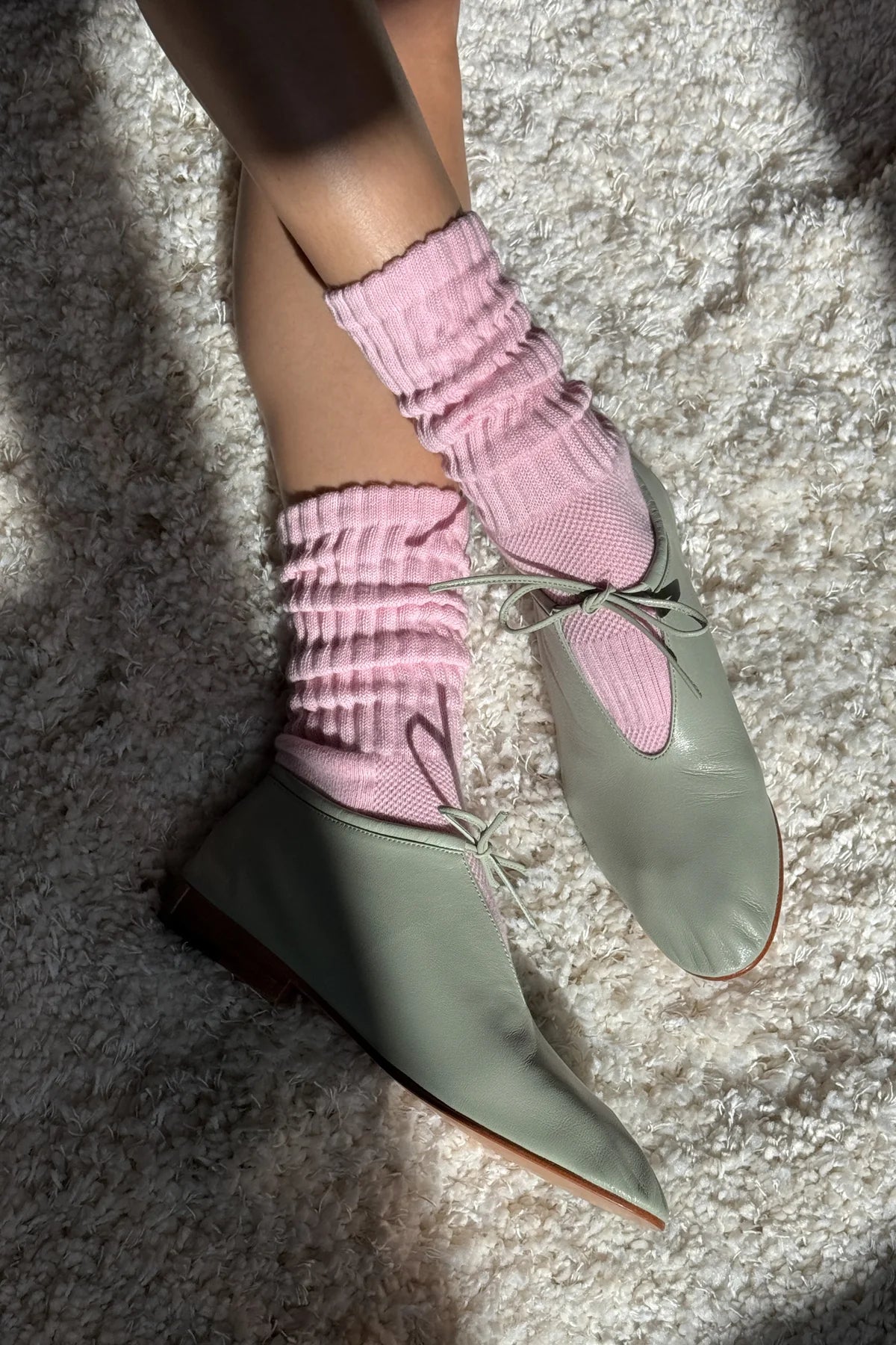 Green pointed-toe shoes with pink ribbed socks on a textured surface