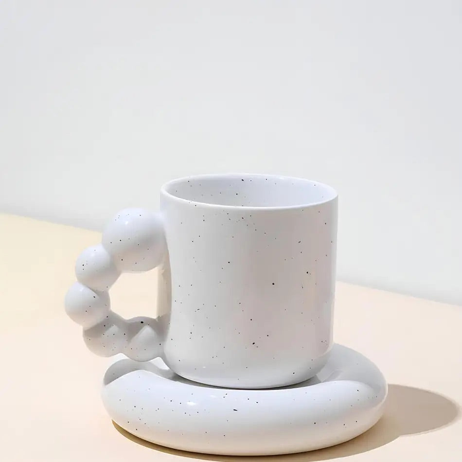 Speckled white ceramic mug and coaster set on a light background